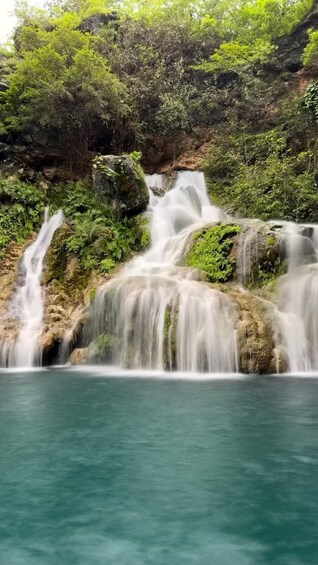 A waterfall cascading over rocks into a clear blue pool surrounded by lush greenery. 1