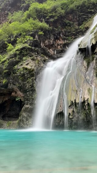 A waterfall cascading into turquoise water surrounded by rocky cliffs and lush greenery. 5