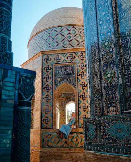 A person sitting on a ledge of a building with intricate tile work and a dome structure. 4