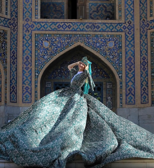 A person in traditional attire in front of a building with intricate blue and beige tile patterns. 1
