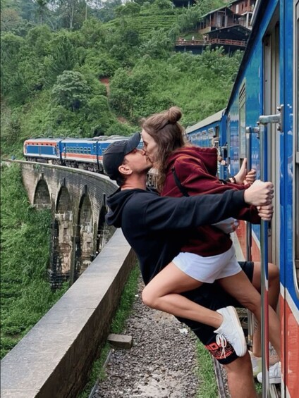 Ein Paar küsst auf einer Eisenbahnbrücke, im Hintergrund ein Zug. 1