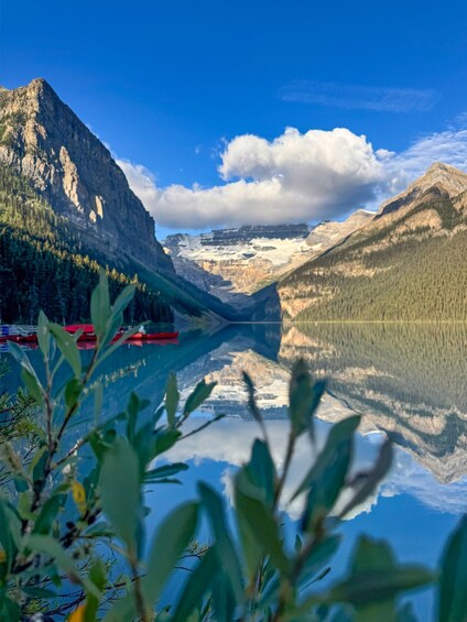 A mountain lake with a red boat, surrounded by forested mountains and clear blue sky. 3