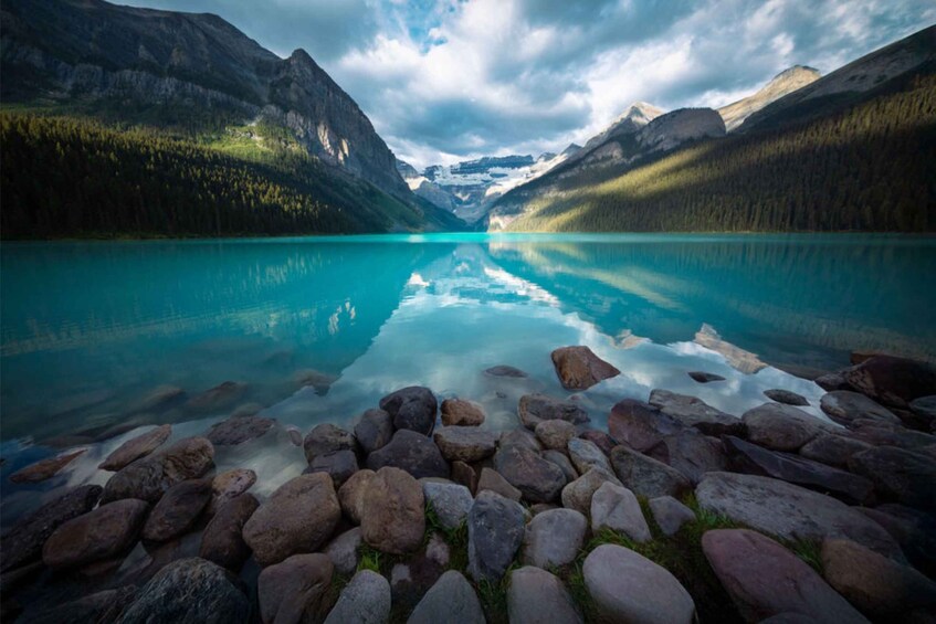 A mountain lake with clear turquoise water, surrounded by rocky shores and forested mountains. 4