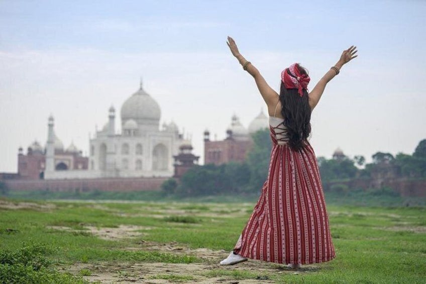 Eine Person steht mit erhobenen Armen in einem Feld und blickt auf den Taj Mahal. 2