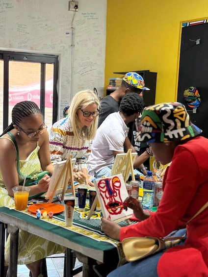 People painting at a table with art supplies and a whiteboard in the background. 1