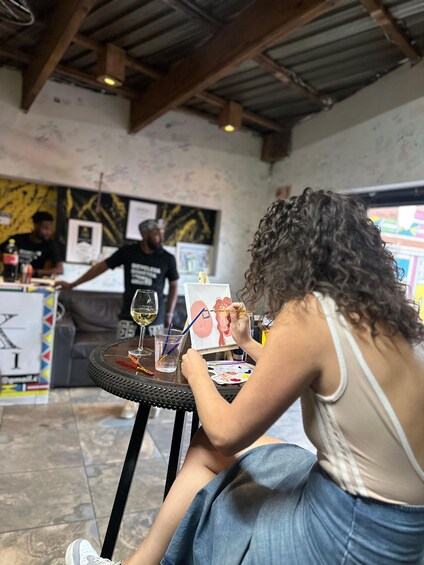 A person painting at a table with a wine glass and palette. 3