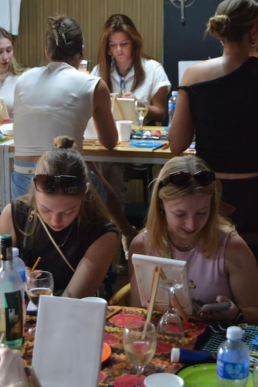 A group of people seated at a table with a bottle of wine, glasses, and a laptop. 3