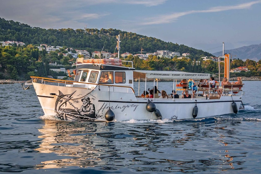 A boat named 'Hemingway' with a mural of a man fishing, sailing on water with a coastal town and hills in the background. 2