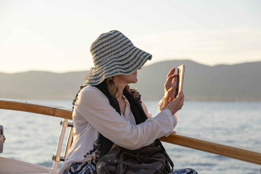 A person sitting on a boat, wearing a striped hat, looking at a smartphone. 1