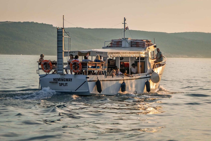 A boat named Hemingway Split on a body of water with people on board. 3