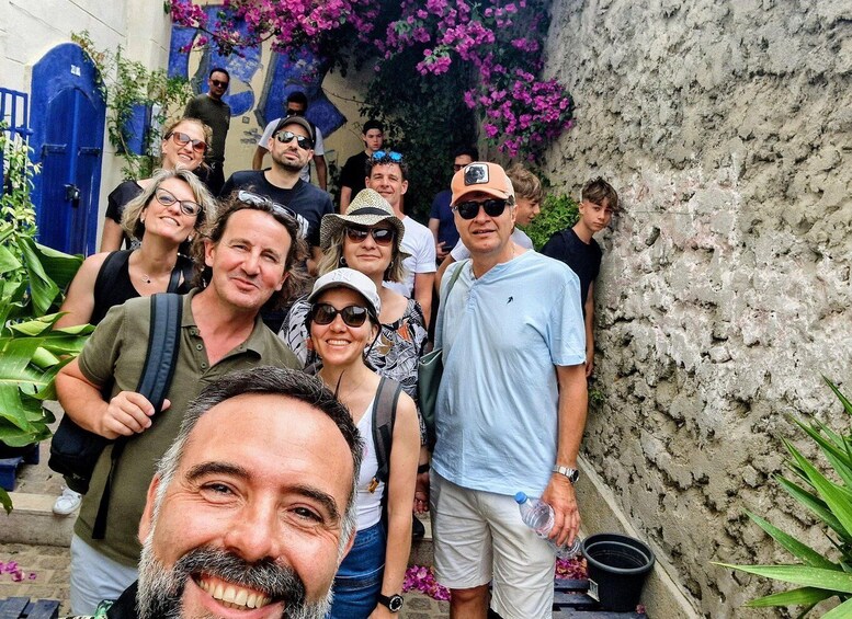 A group of people standing on a street with a blue gate and pink flowers in the background. 1