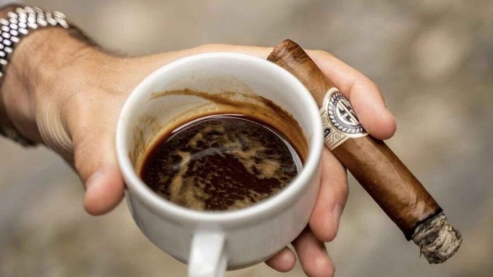 A hand holding a cup of coffee and a cigar. 1