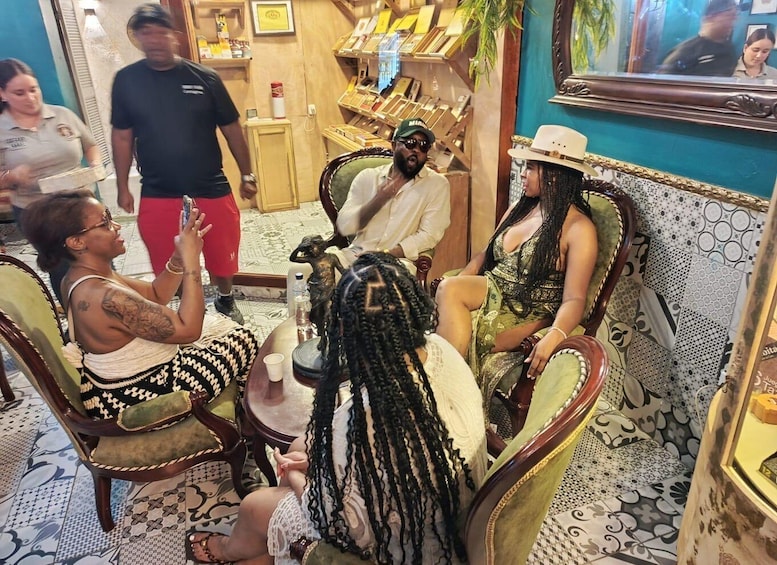 A group of people seated around a table in a room with patterned floor tiles and ornate chairs. 3