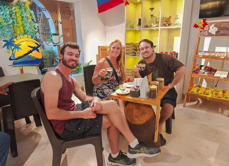 Three people seated at a wooden table in a café with a mural and shelves of snacks in the background. 2