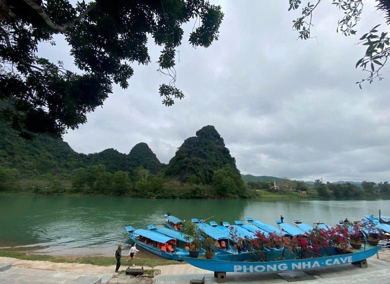 A boat named 'PHONG NHA CAVE' docked at a riverbank with a forested landscape and mountains in the background. 1