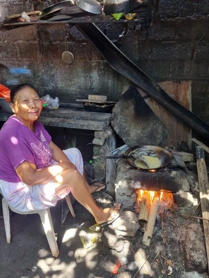 A person sitting by a traditional outdoor cooking stove with pots and pans. 2