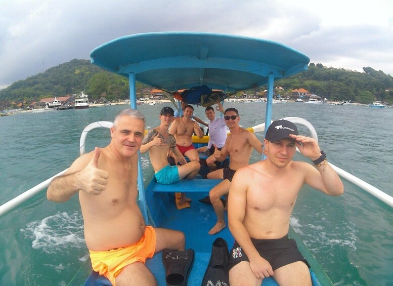 A group of people on a boat with a blue canopy, surrounded by water and a hilly landscape in the background. 5