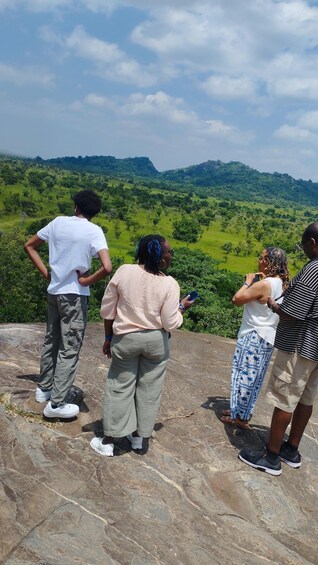 Four people standing on a rocky outcrop overlooking a lush green landscape with hills in the distance. 1