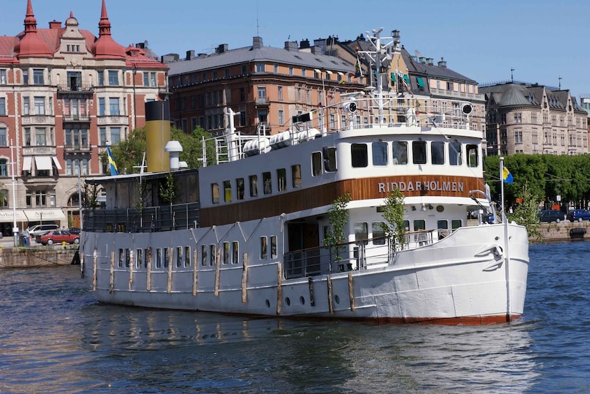 A white and brown riverboat named Riddarholmen sailing on a river. 1