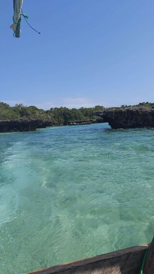 A boat on clear turquoise water with a rocky coastline and dense greenery in the background. 4