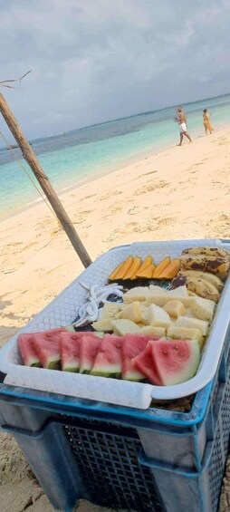 A beach with a cooler containing fruits and a person walking in the background. 5