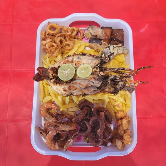 A tray of seafood including fried calamari, grilled fish, shrimp, and octopus, served with fries and garnished with lime slices. 3