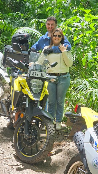 A yellow motorcycle with a license plate, parked in a lush green area. 2