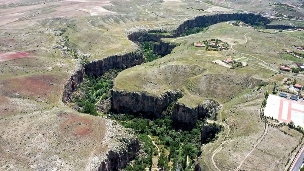 A rugged landscape with a deep canyon, green vegetation, and scattered buildings. 1