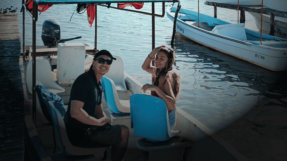 A man and a woman on a boat docked at a marina with other boats in the background. 3