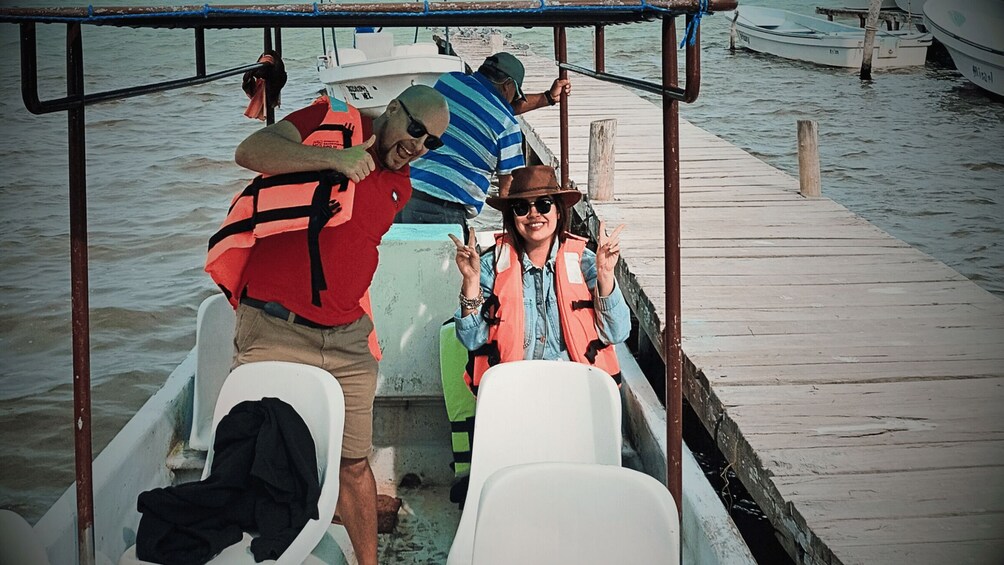 A boat with two people wearing life jackets, one in a red shirt and the other in a striped shirt, on a wooden dock. 5