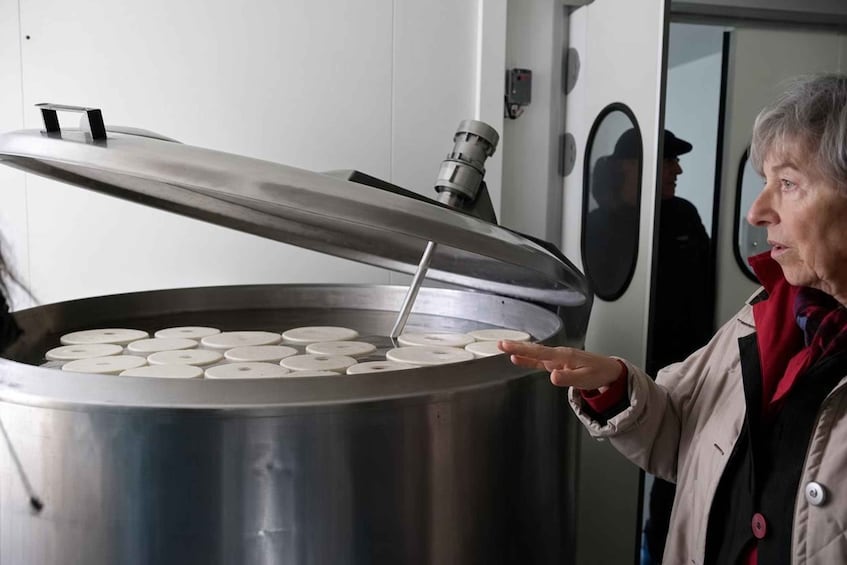 En person som interagerar med en stor industriell maskin, eventuellt en matberedare, där locket är öppet och avslöjar cirkelformade komponenter inuti. 2