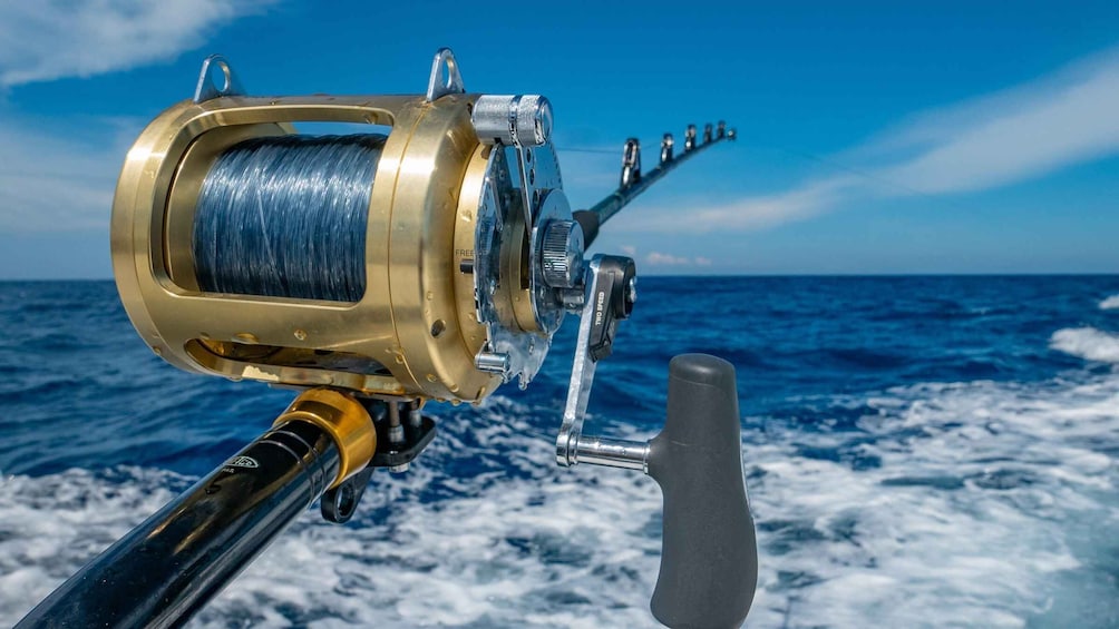 A fishing reel with a gold-colored handle and a black handle, set against a backdrop of the ocean. 1