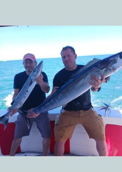 Two people holding large fish on a boat with the ocean in the background. 5