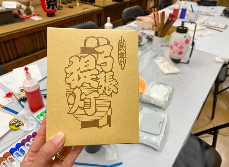 A hand holding a brown card with Chinese characters and a drawing of a teapot. 3