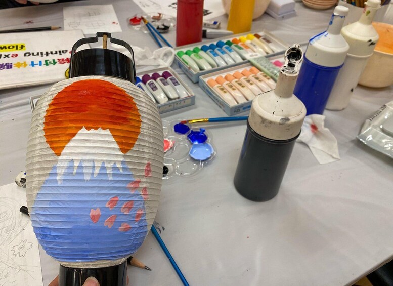 A lamp with a painted design, paint bottles, and art supplies on a table. 5