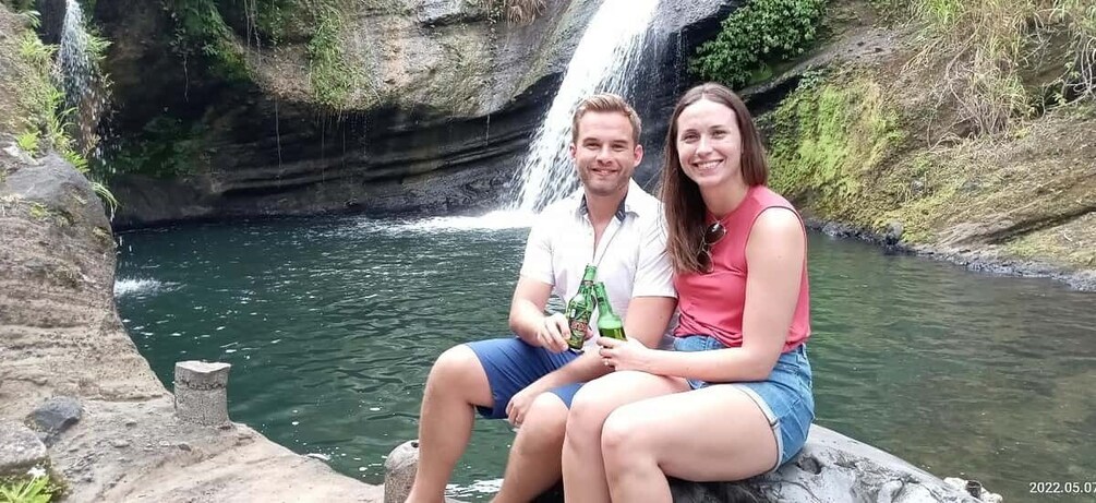 Two people sitting by a waterfall. 1