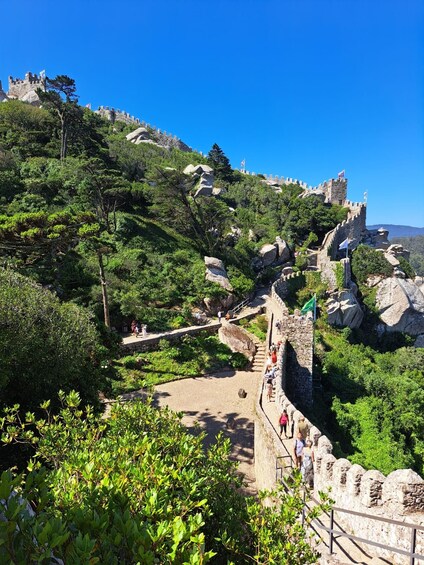 Un castello storico su una collina, con un percorso pedonale lastricato e visitatori. 5
