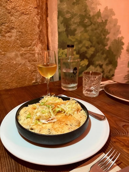 A meal with a glass of white wine, a bottle of water, and a fork on a wooden table. 5