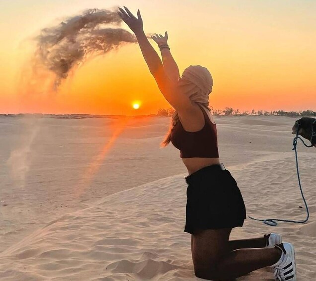A person kneeling on sand dunes at sunset with a dog on a leash. 1