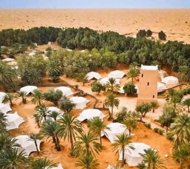 A desert landscape with palm trees, white tents, and a central building. 1