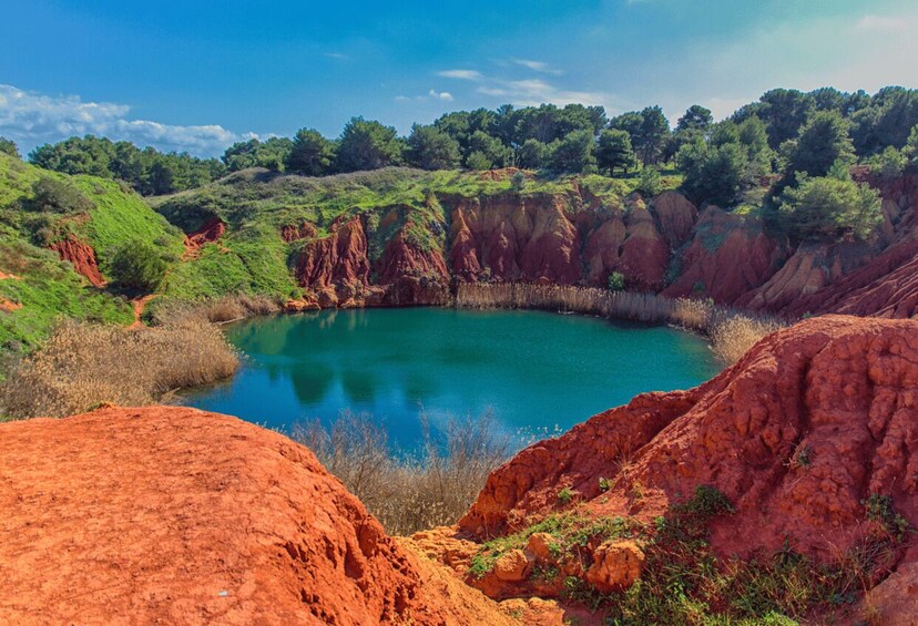 A natural landscape with a turquoise lake surrounded by reddish-brown cliffs and green vegetation. 4