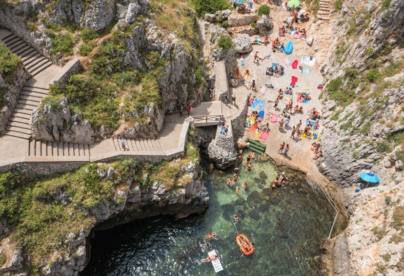 A rocky beach with clear water, a small boat, and people sunbathing. 5