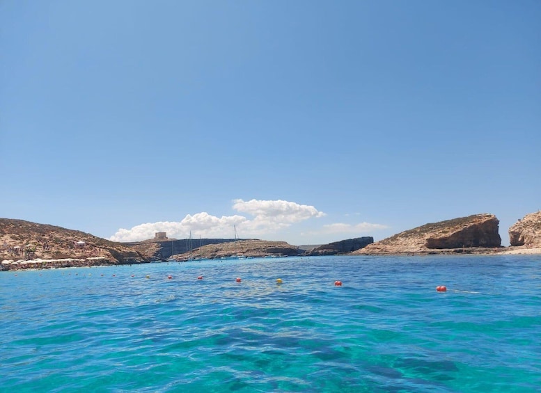 A coastal landscape with clear blue waters, rocky outcrops, and a distant building on a hill. 3