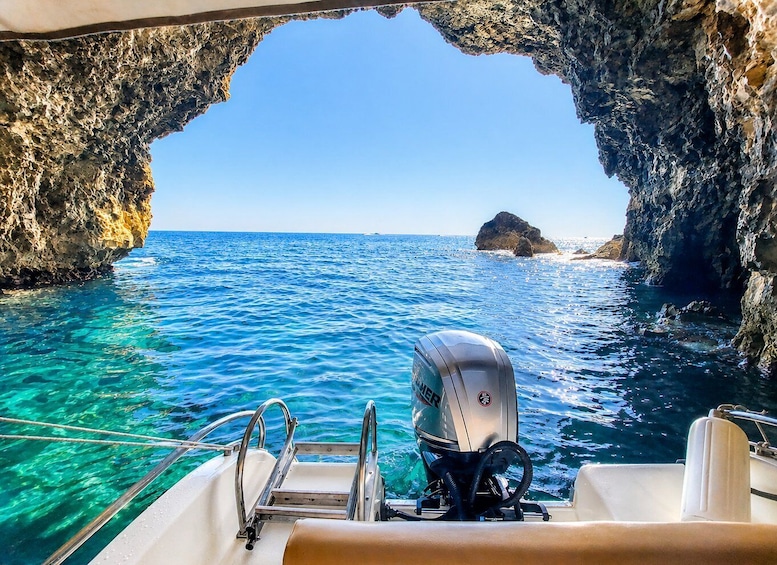 A boat navigating through a rocky arch with clear blue waters and a distant island. 2