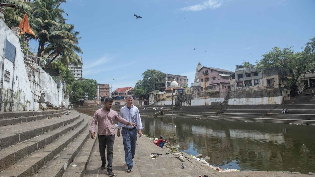 A riverside walkway with steps leading down to the water, surrounded by buildings and palm trees. 2