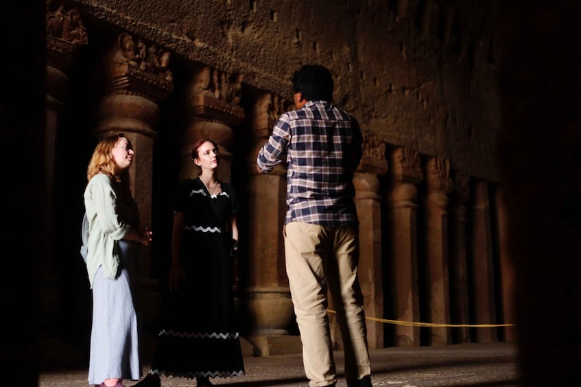 A person taking a photo of two individuals in a dimly lit historical building with stone columns. 1