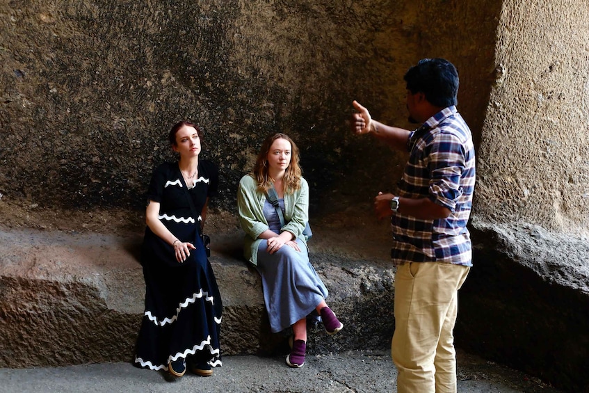 Three people sitting on a stone ledge in a rocky outdoor setting. 3