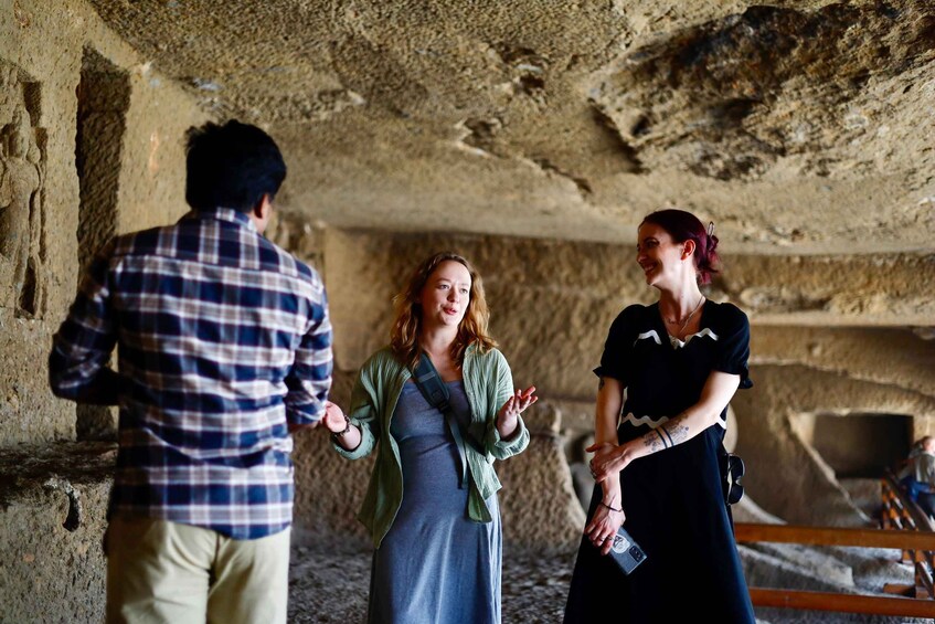 Three people in a cave with rough stone walls and a wooden bench. 1