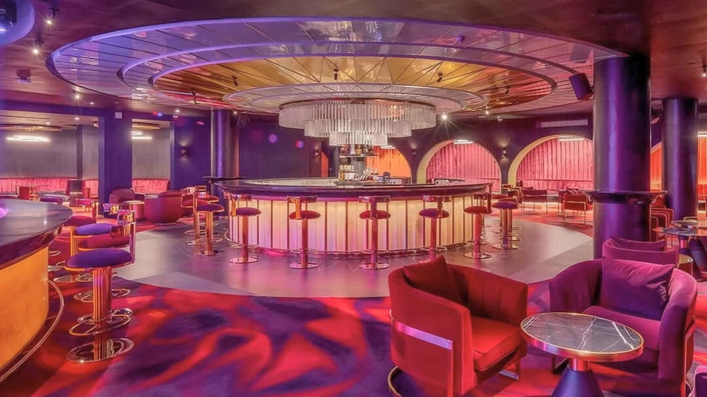 A modern bar with a circular bar area, red seating, and a chandelier. 3