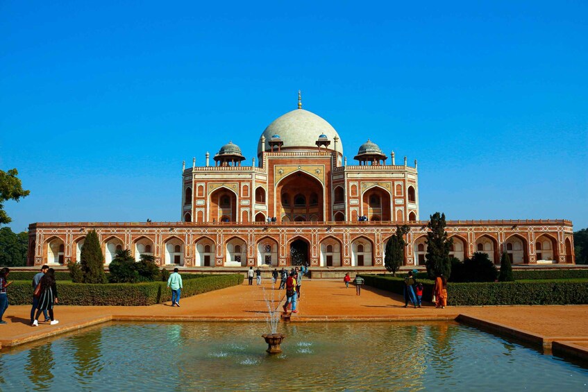 A large, ornate building with a central dome and arched windows, surrounded by a water feature and visitors. 1